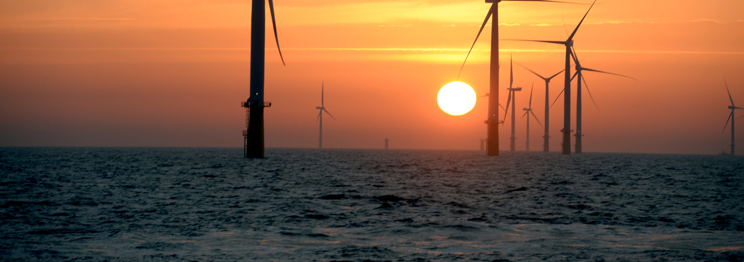 A photo of an offshore wind farm in sunset