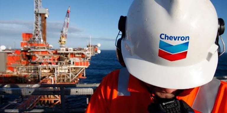Man with a hardhat with words "Chevron" on it with an offshore rig in the background
