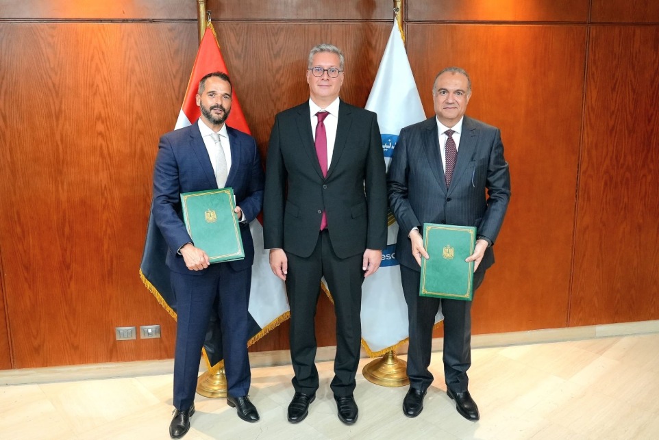 Three men holding documents in front of two flags