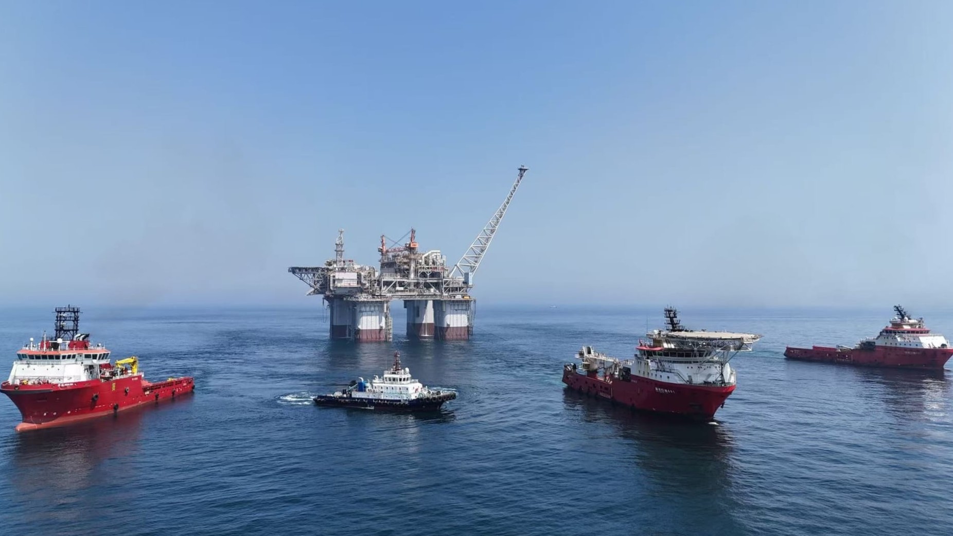 A large offshore platform surrounded by several smaller boats